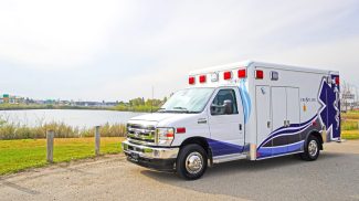 Crestline CCL 166 ambulance parked beside a river under a bright sky, showcasing its clean design and reflective graphics