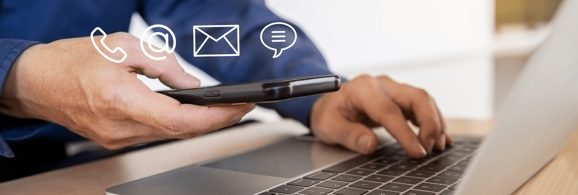 Person holding a smartphone while typing on a laptop, with contact icons for phone, email, and chat displayed above to represent communication options.