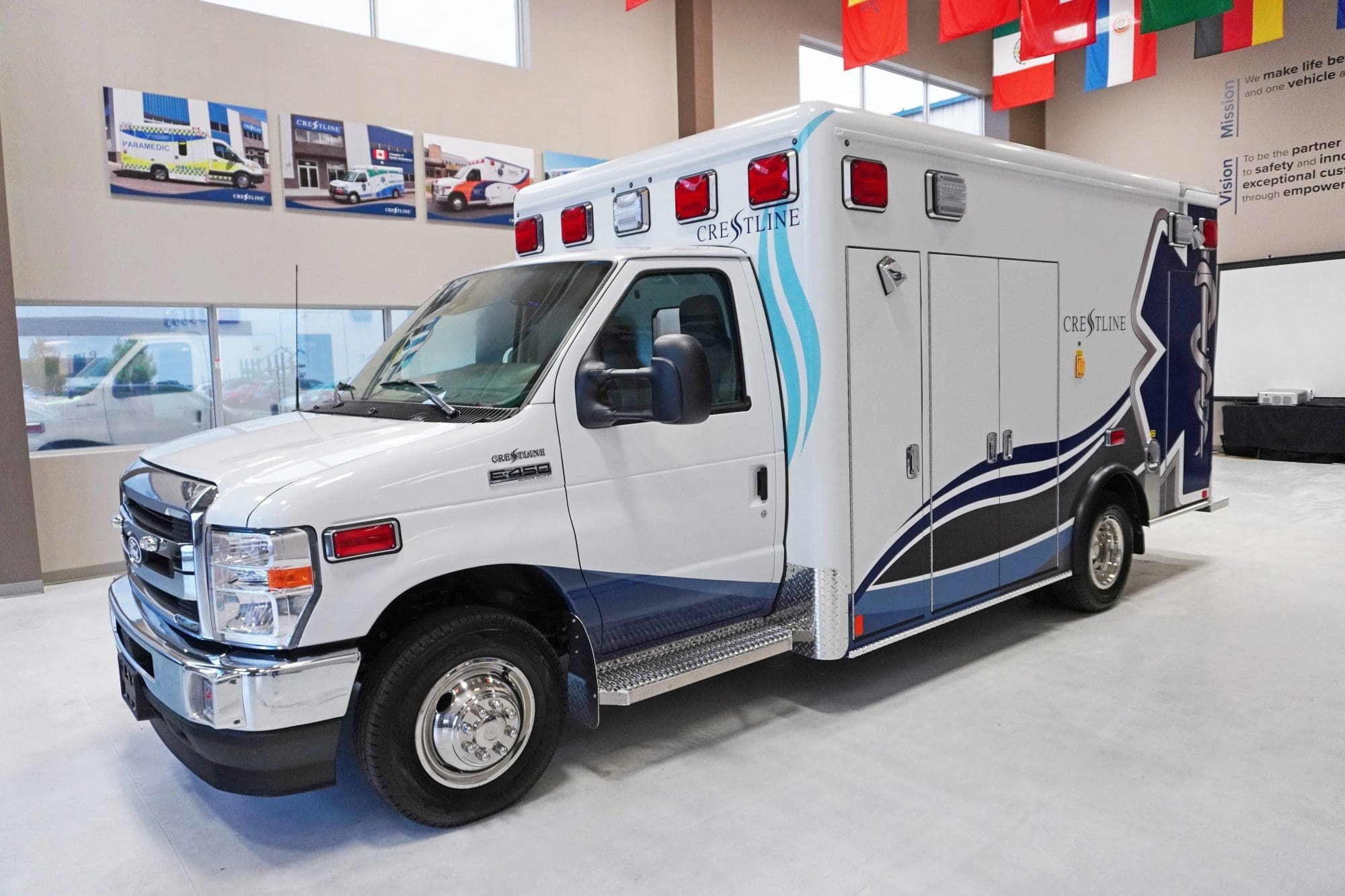 Crestline ambulance on a Ford E-450 chassis, shown indoors with white and blue graphics, red emergency lights, and the Crestline logo