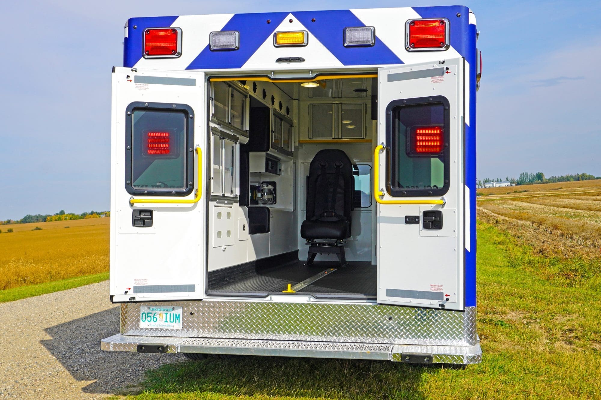 Rear view of a Crestline ambulance with its back doors open, showcasing the clean and organized patient care interior against a rural field backdrop