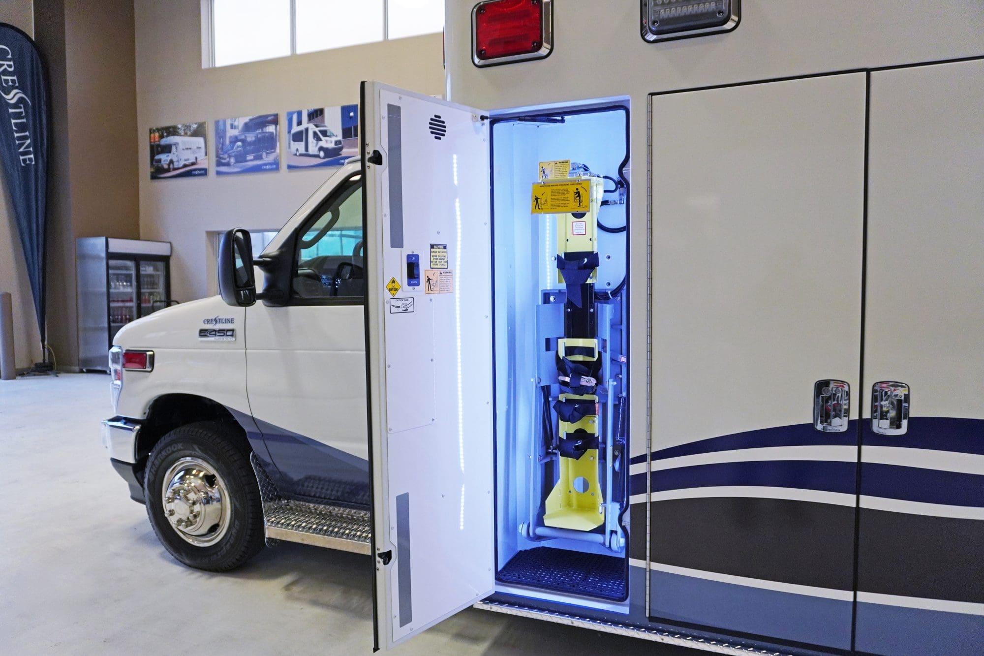 Side compartment of a Crestline ambulance with an integrated yellow oxygen cylinder lift system securely stowed inside, highlighted by bright interior lighting for clear visibility and accessibility