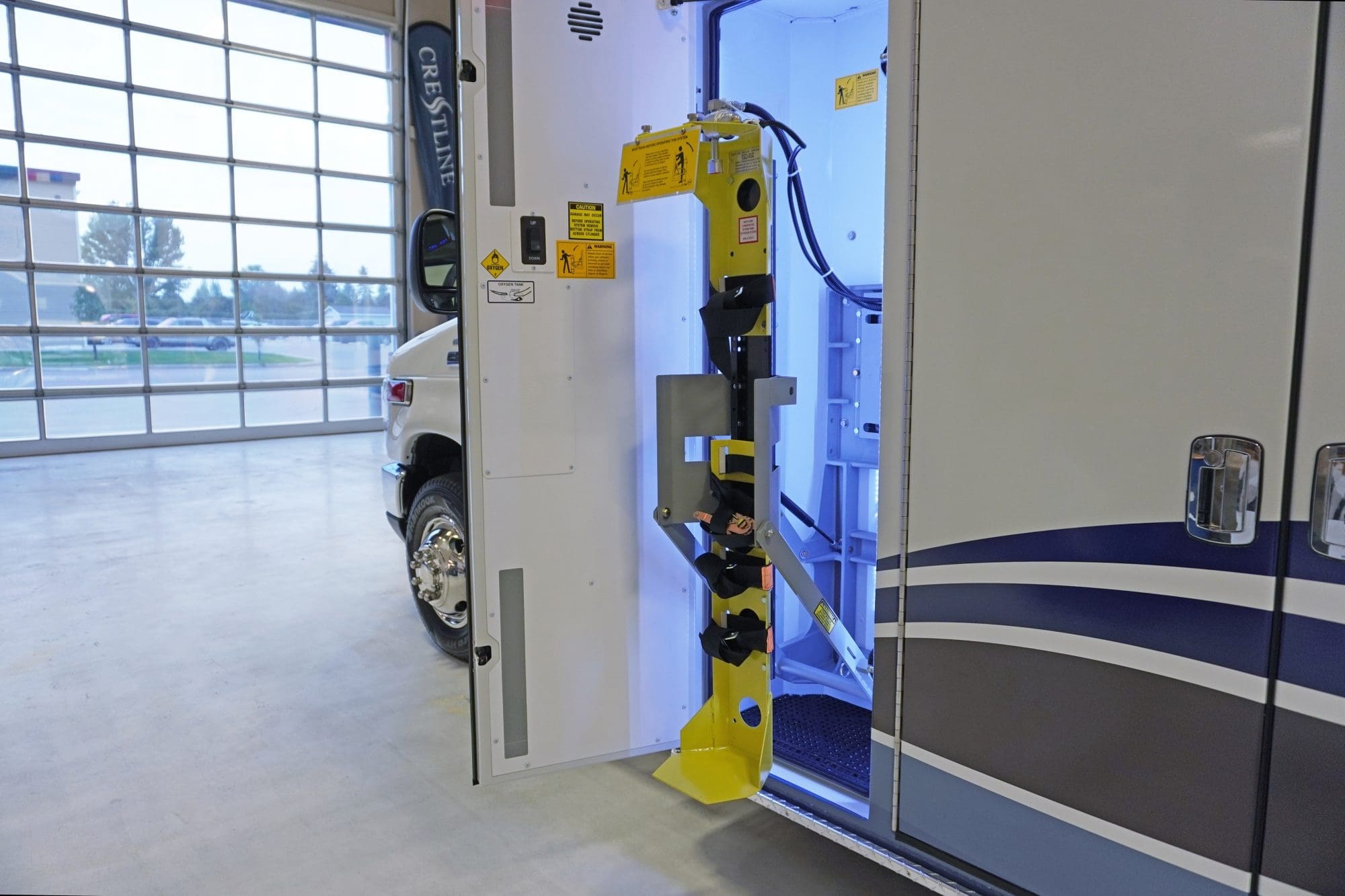 Extended yellow oxygen cylinder lift system mounted inside a Crestline ambulance side compartment, illuminated by interior LED lighting