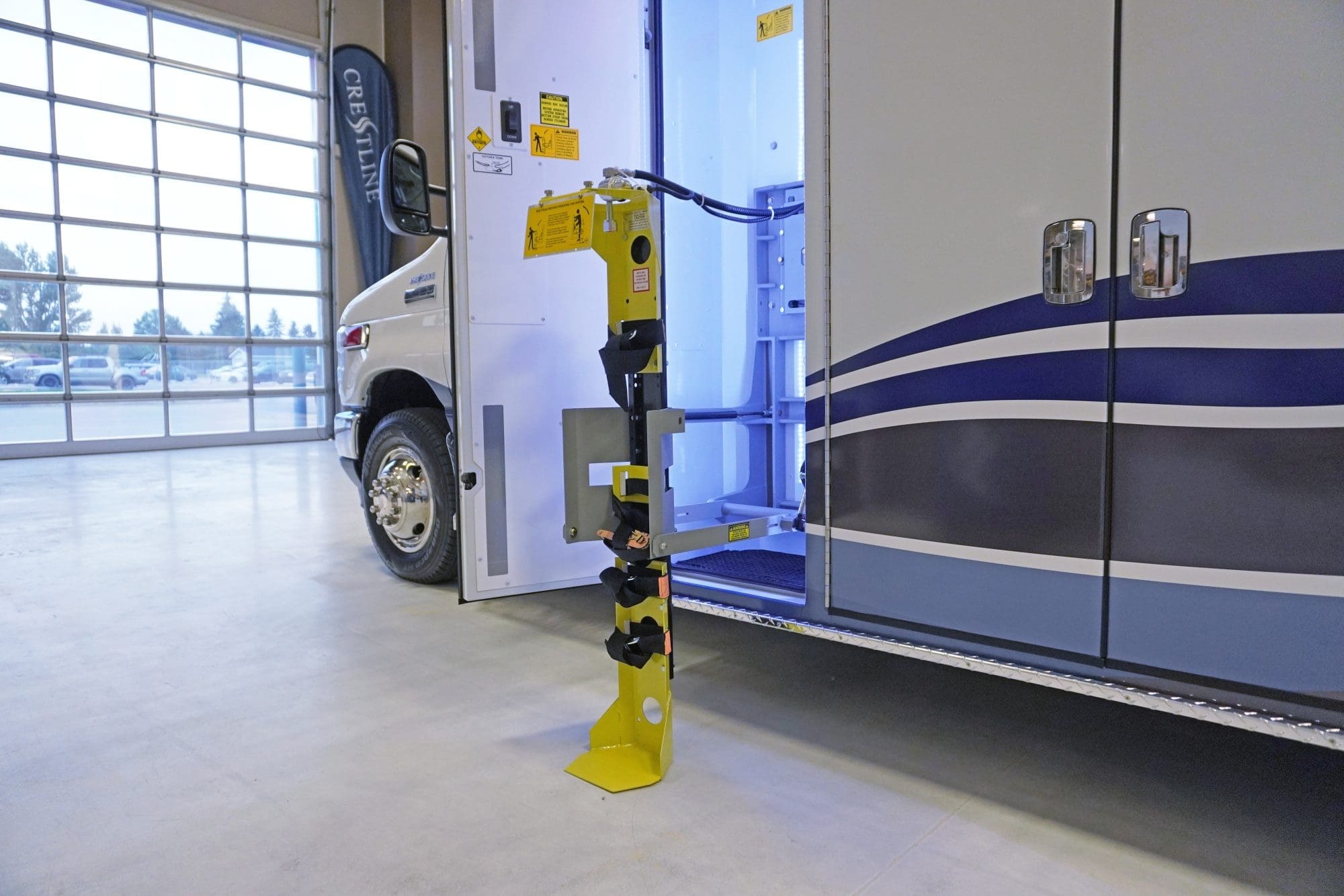 Side compartment of a Crestline ambulance open to reveal a mounted yellow oxygen cylinder bracket system, shown extended for maintenance or access, with interior lighting illuminating the storage area