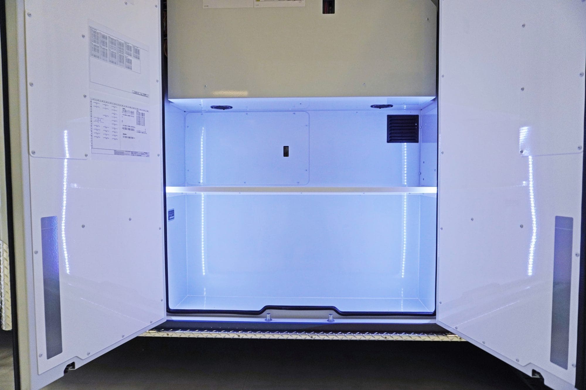 Open exterior storage compartment of a Crestline ambulance, featuring bright LED lighting, a two-tier shelf layout, and a clean white interior
