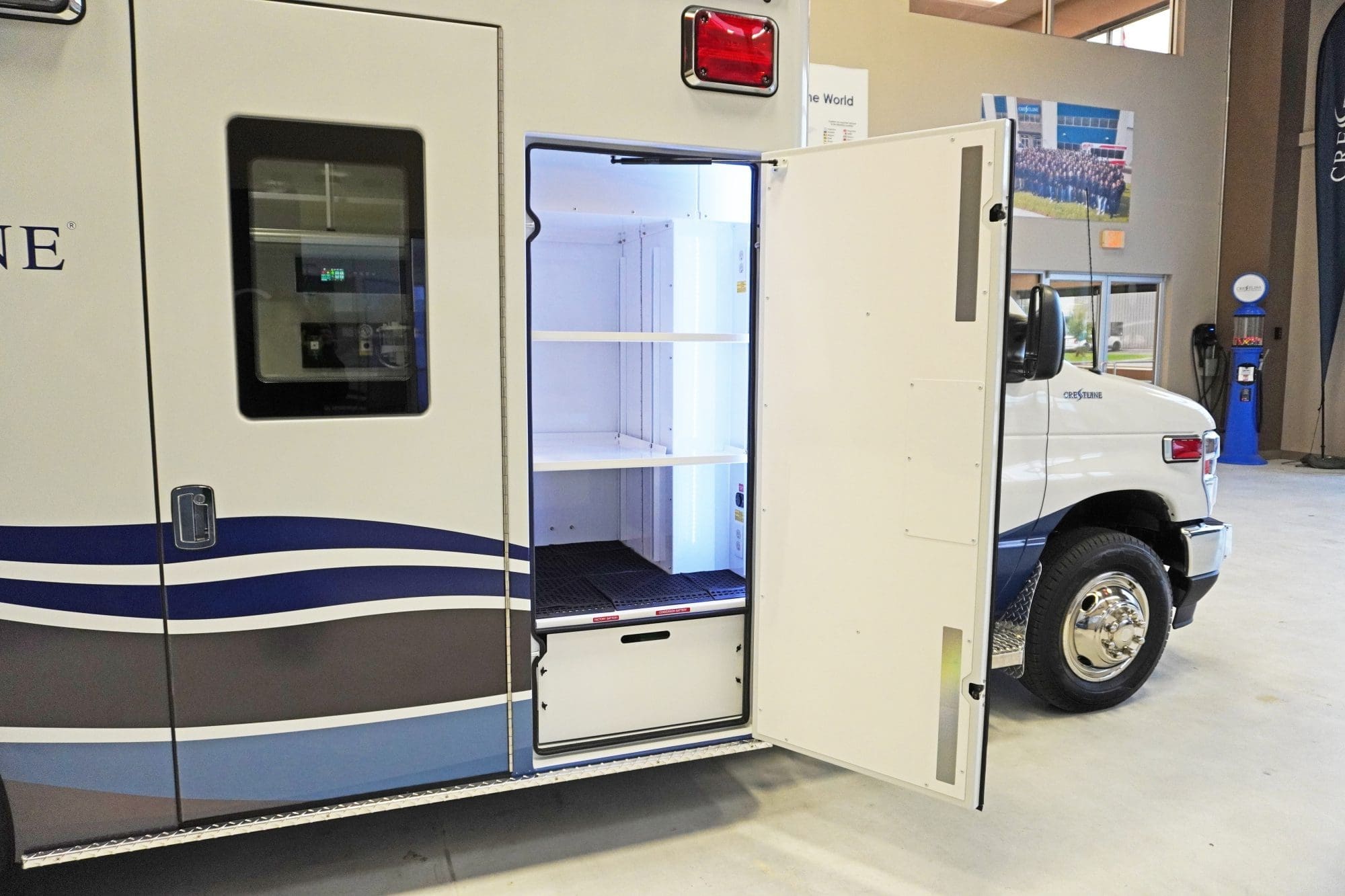 Exterior view of a Crestline ambulance with a side compartment door open, revealing illuminated interior shelving designed for organized storage of medical equipment and supplies