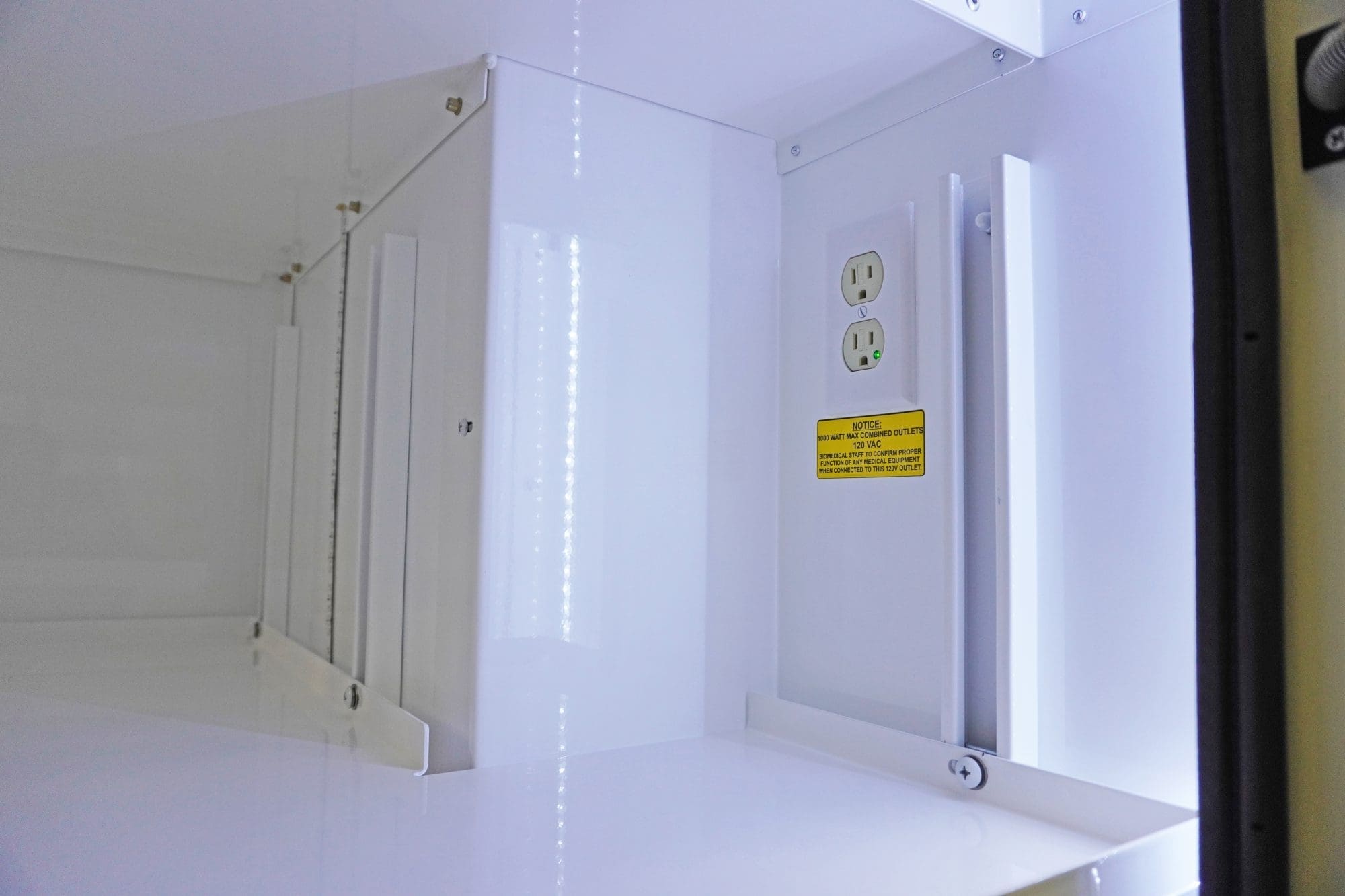 Close-up view of an illuminated Crestline ambulance storage compartment with clean white surfaces, integrated electrical outlets, and a safety notice label