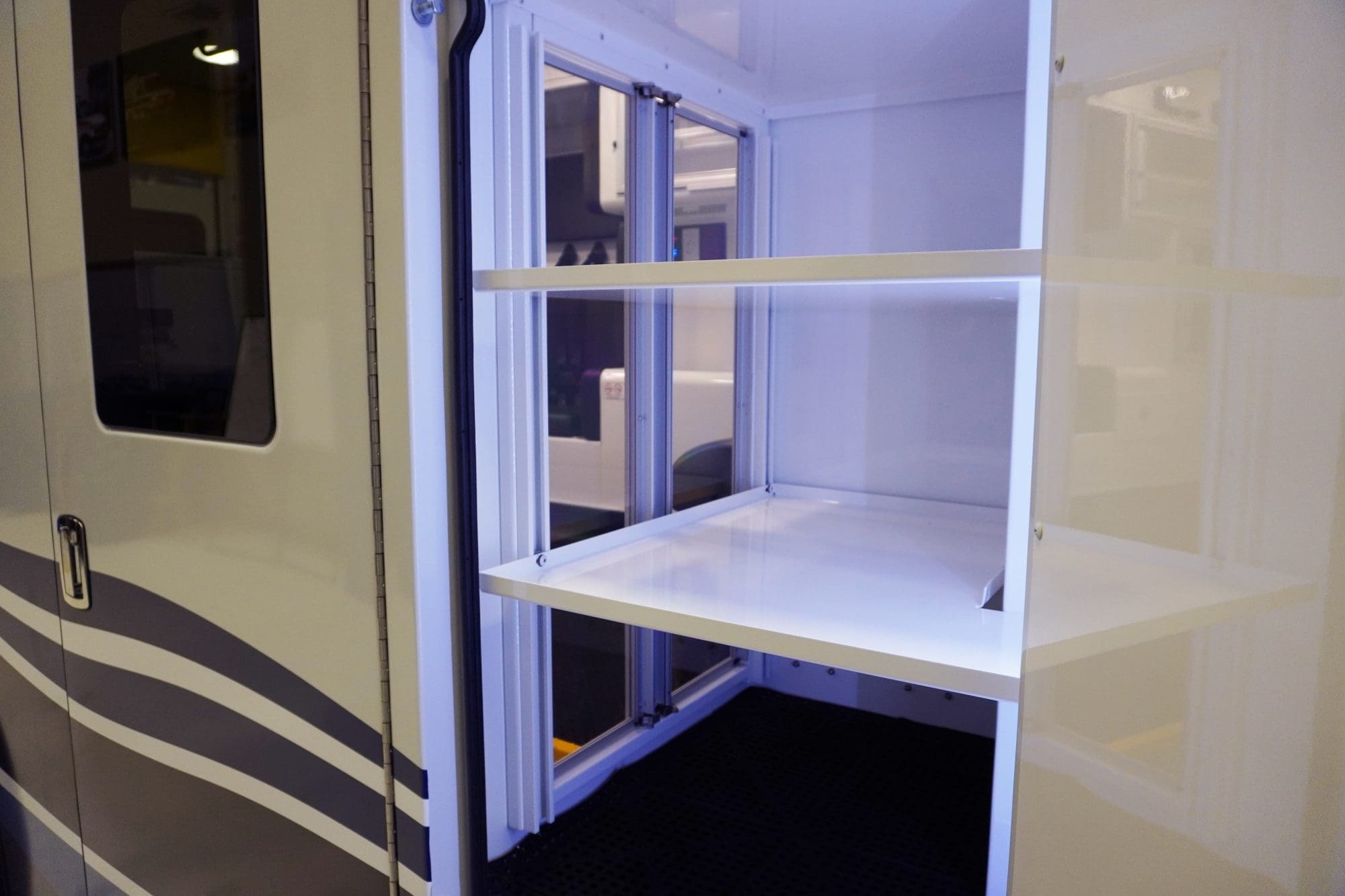 Interior cabinet inside a Crestline ambulance with adjustable white shelving and sliding clear doors, illuminated to showcase organized storage space for medical equipment and supplies