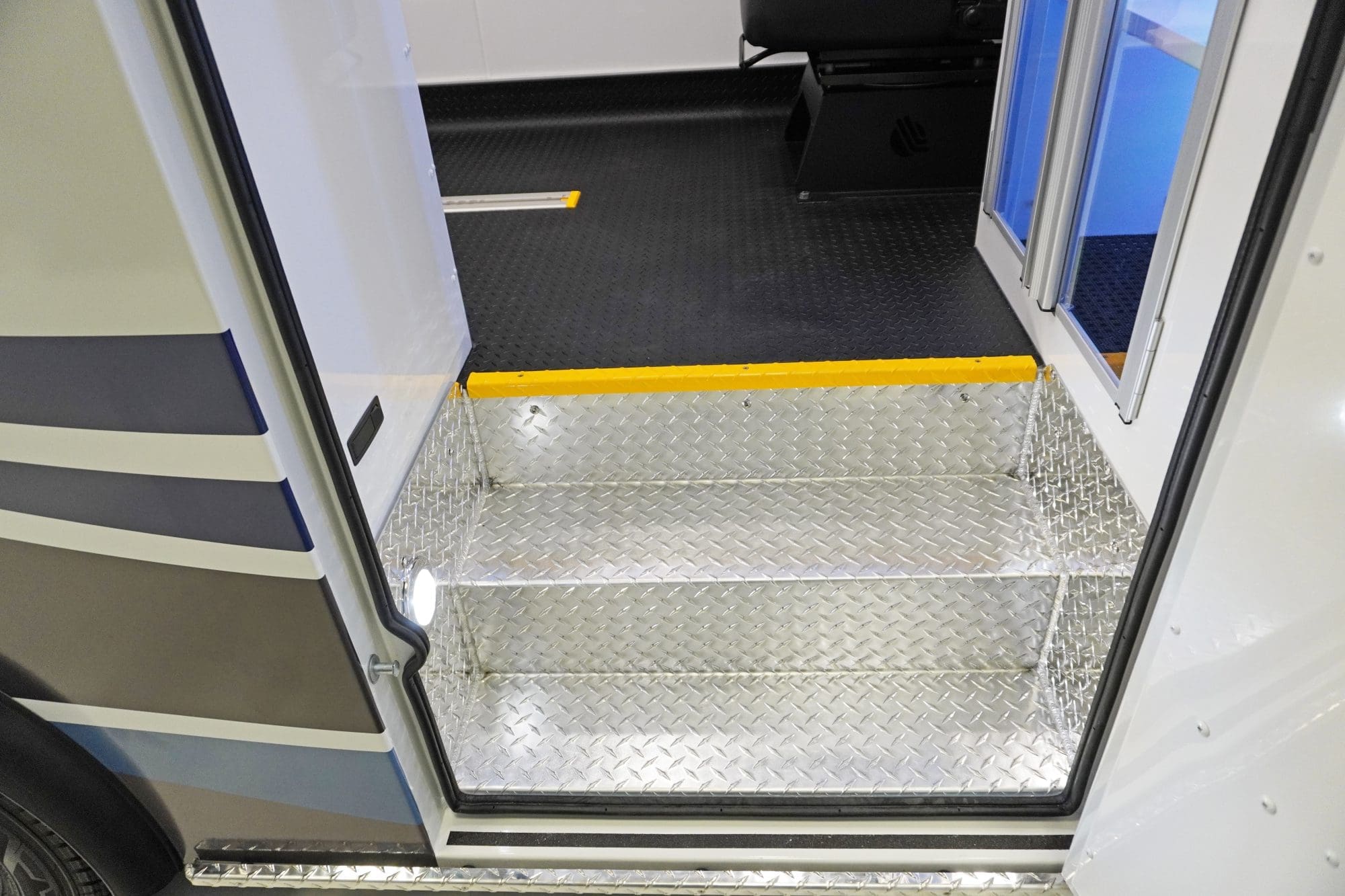 Entry step of a Crestline ambulance featuring diamond plate aluminum flooring with integrated lighting and a yellow safety edge