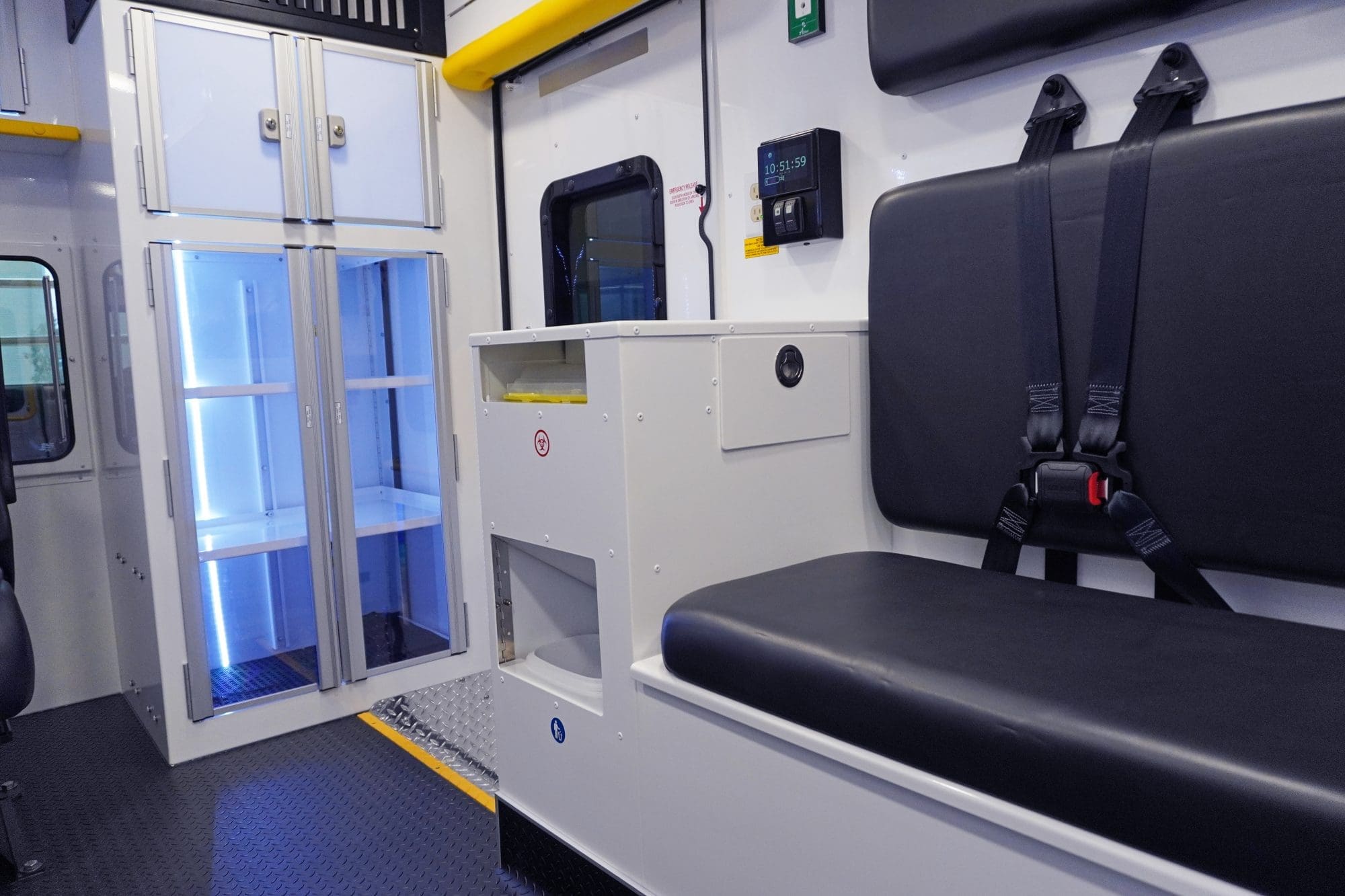 Crestline ambulance interior featuring a black bench seat with seatbelts, illuminated storage cabinets, a biohazard waste disposal unit, and a digital control panel