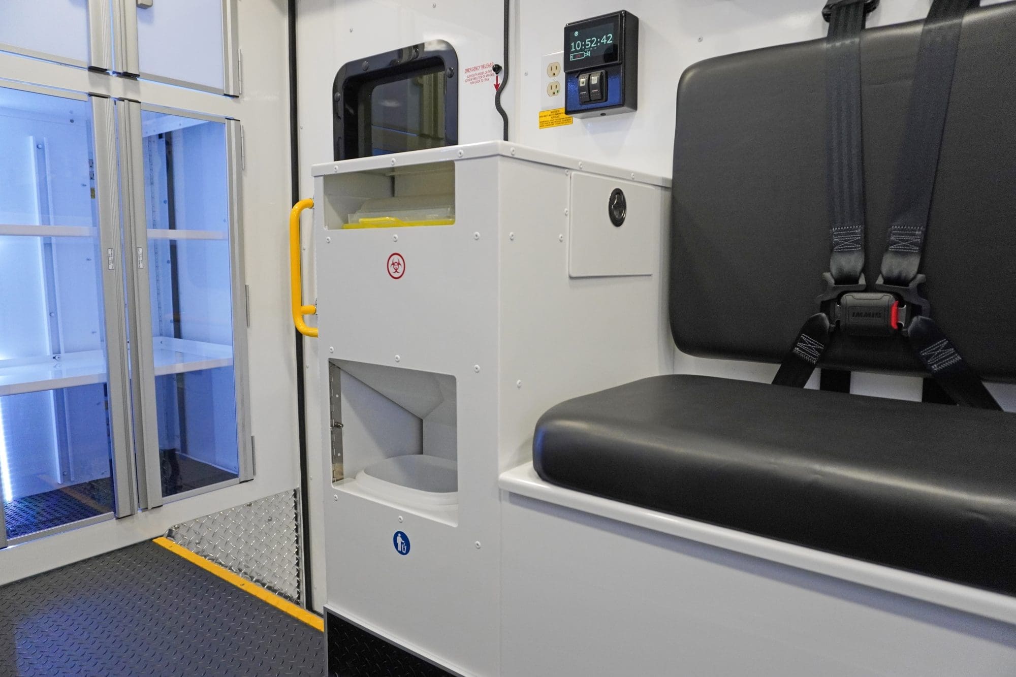 Interior of a Crestline ambulance featuring a black bench seat with seatbelts, a biohazard waste disposal unit, illuminated storage cabinets, and a digital control panel with power outlets