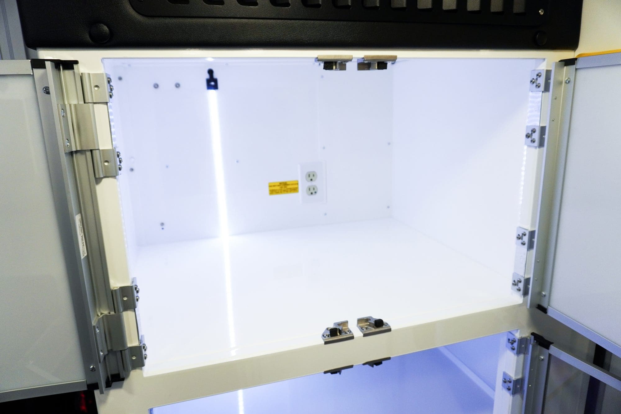 Close-up view of an illuminated interior Crestline ambulance cabinet with white shelving, clear doors, and built-in electrical outlets