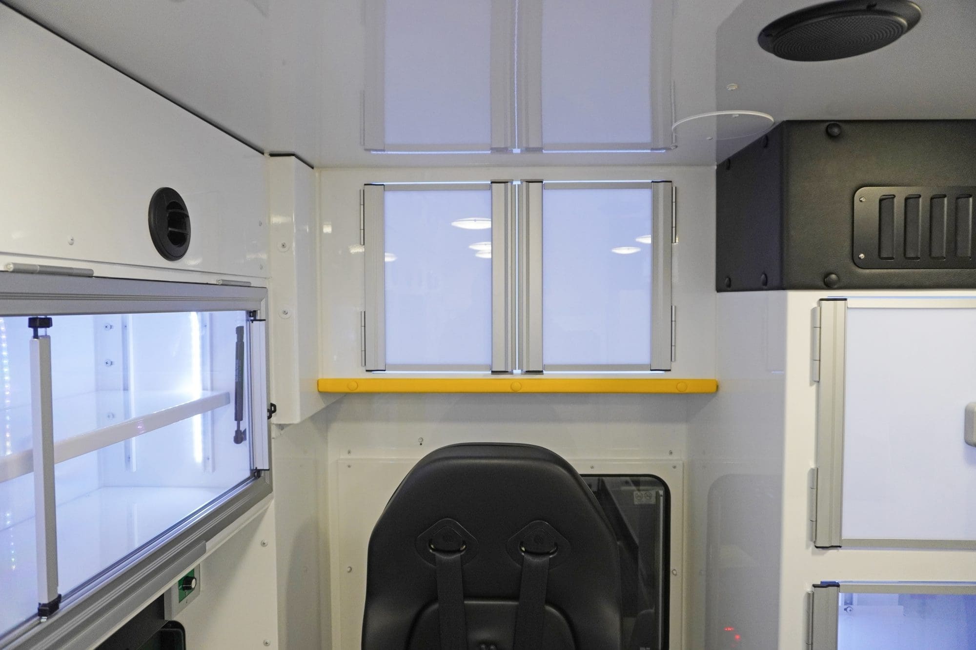 Interior view of a Crestline ambulance showing closed upper storage cabinet doors above the attendant seat, with a yellow safety rail and adjacent LED-lit aluminum cabinets along the side wall