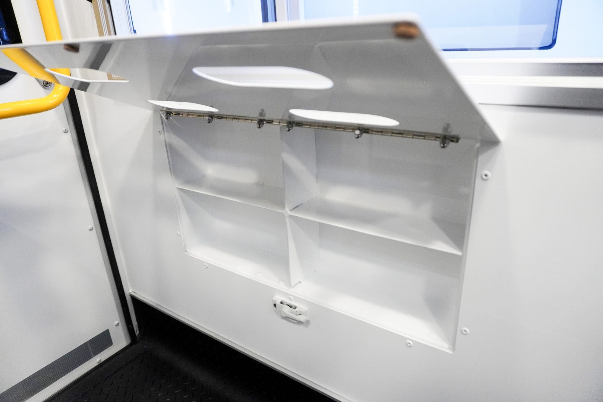 Open lower storage compartment inside a Crestline ambulance, featuring divided shelves and a fold-down access door located beneath the aluminum sliding cabinets