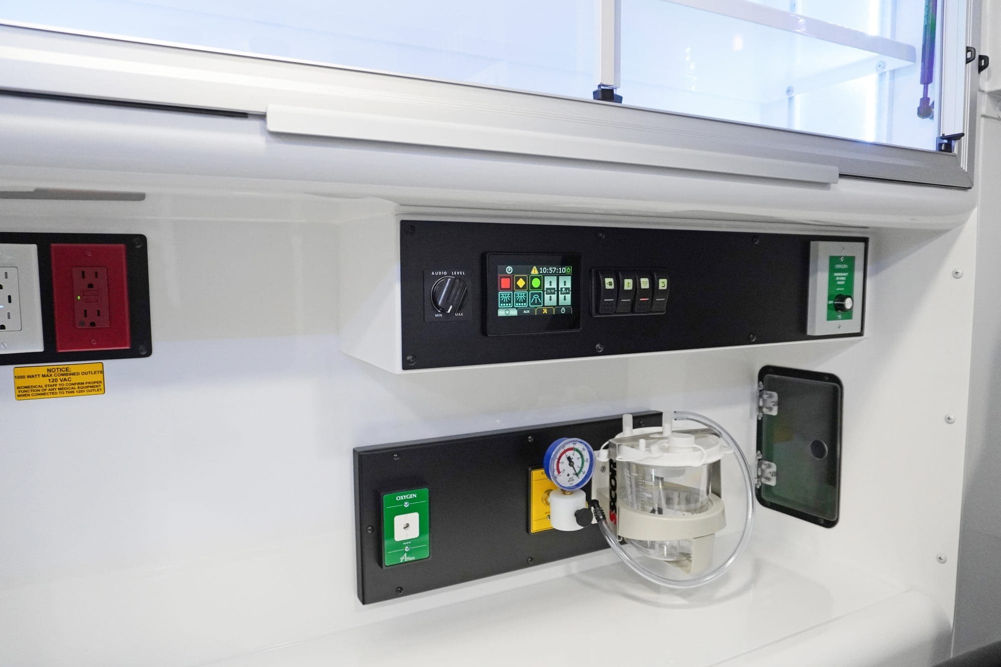 Crestline ambulance interior wall showing the main control panel with touchscreen display, illuminated switches, electrical outlets, oxygen control valves, and onboard suction system for patient care