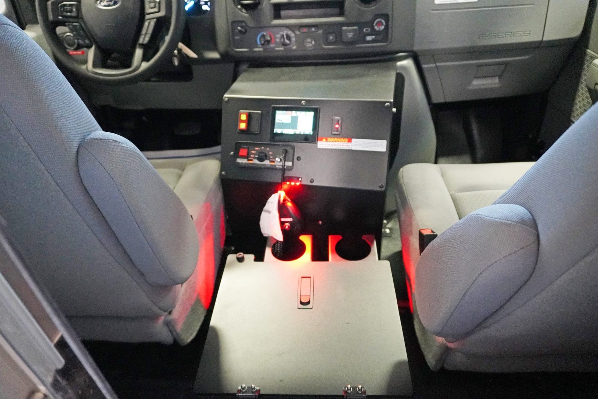 View of the cab console between the driver and passenger seats in a Crestline ambulance, featuring illuminated red lighting, integrated control switches, a touchscreen display, and dual cup holders