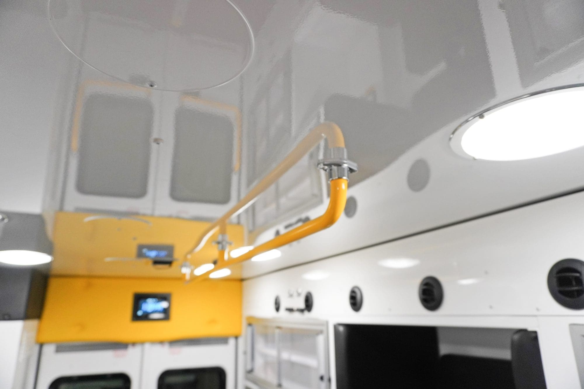 Ceiling-mounted yellow grab rail extending the length of the Crestline ambulance interior, providing stability for EMS personnel during patient transport