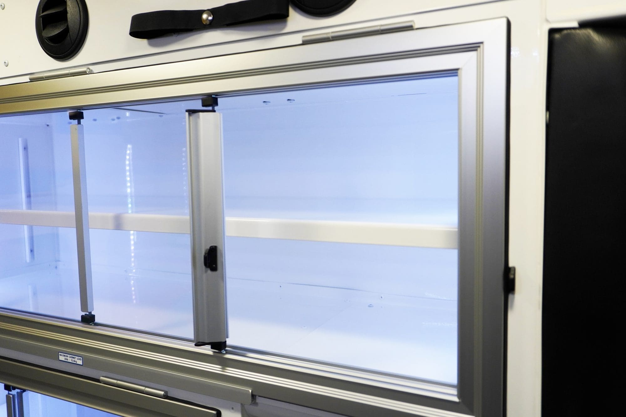 Close-up of an illuminated Crestline ambulance interior cabinet with sliding glass doors, white shelving, and integrated LED lighting along the edges