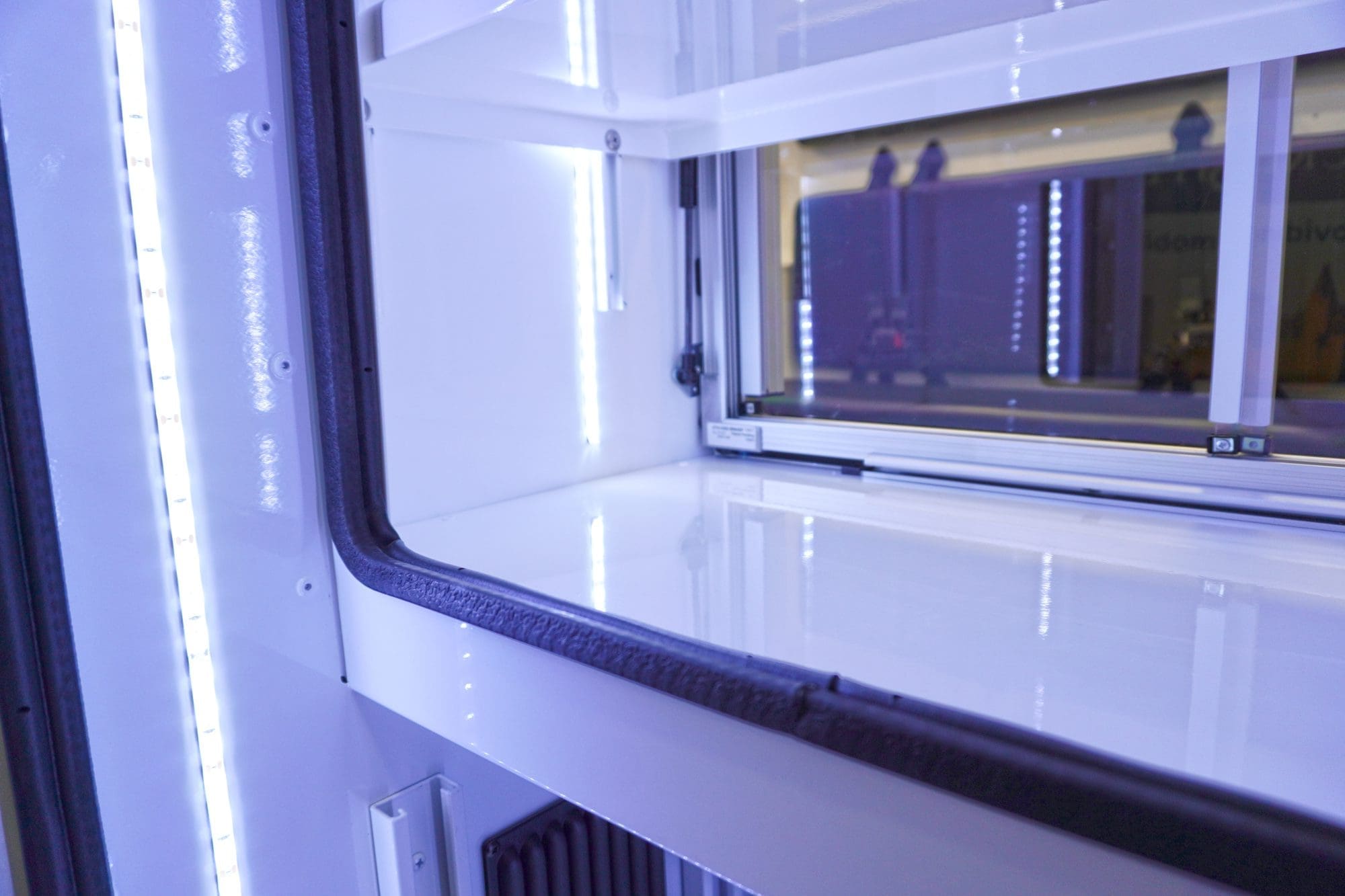 Close-up view of an illuminated Crestline ambulance storage compartment with LED lighting, white shelving, and sliding glass doors framed with black trim