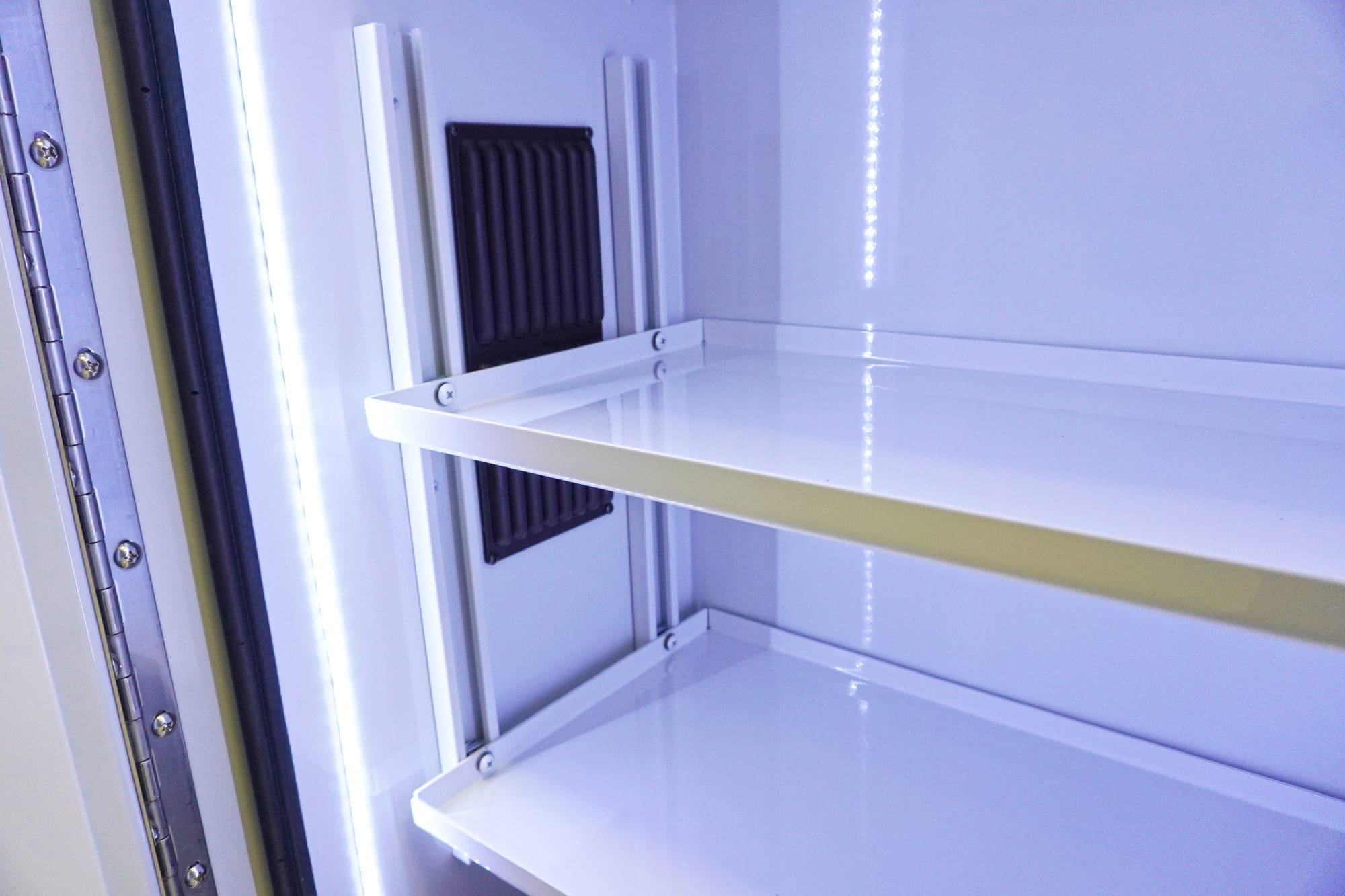 Interior view of an illuminated Crestline ambulance storage cabinet showing smooth white shelving, LED lighting strips, and a black ventilation panel on the back wall