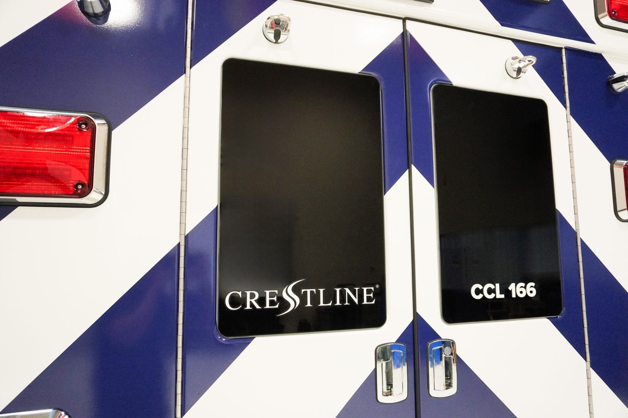Close-up of the rear doors on a Crestline CCL 166 ambulance featuring blue and white chevron graphics, tinted windows, and chrome door handles