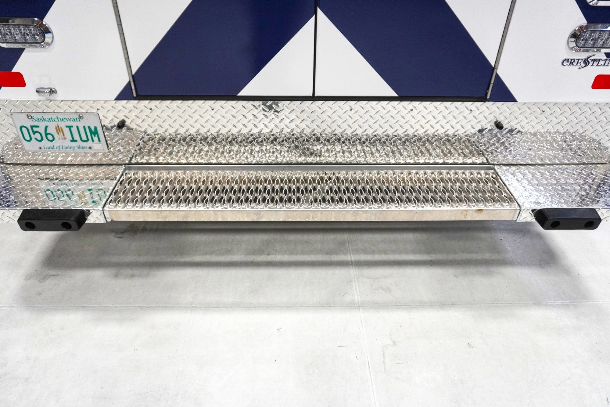 Close-up of a Crestline ambulance rear step bumper with diamond plate aluminum and Saskatchewan license plate