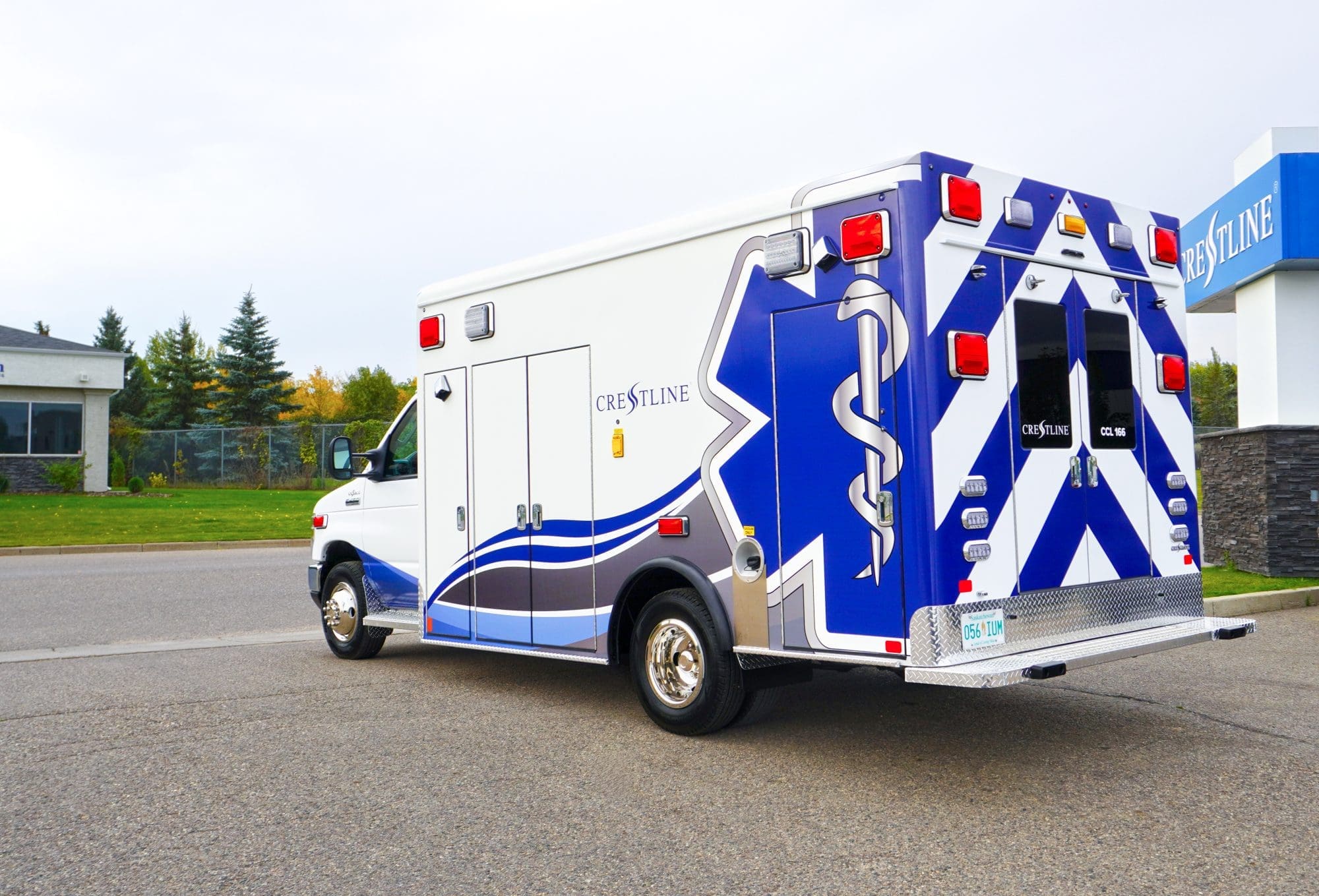 Rear and side view of a Crestline CCL 166 ambulance parked near the Crestline facility, highlighting its bold blue and white graphics and Star of Life design