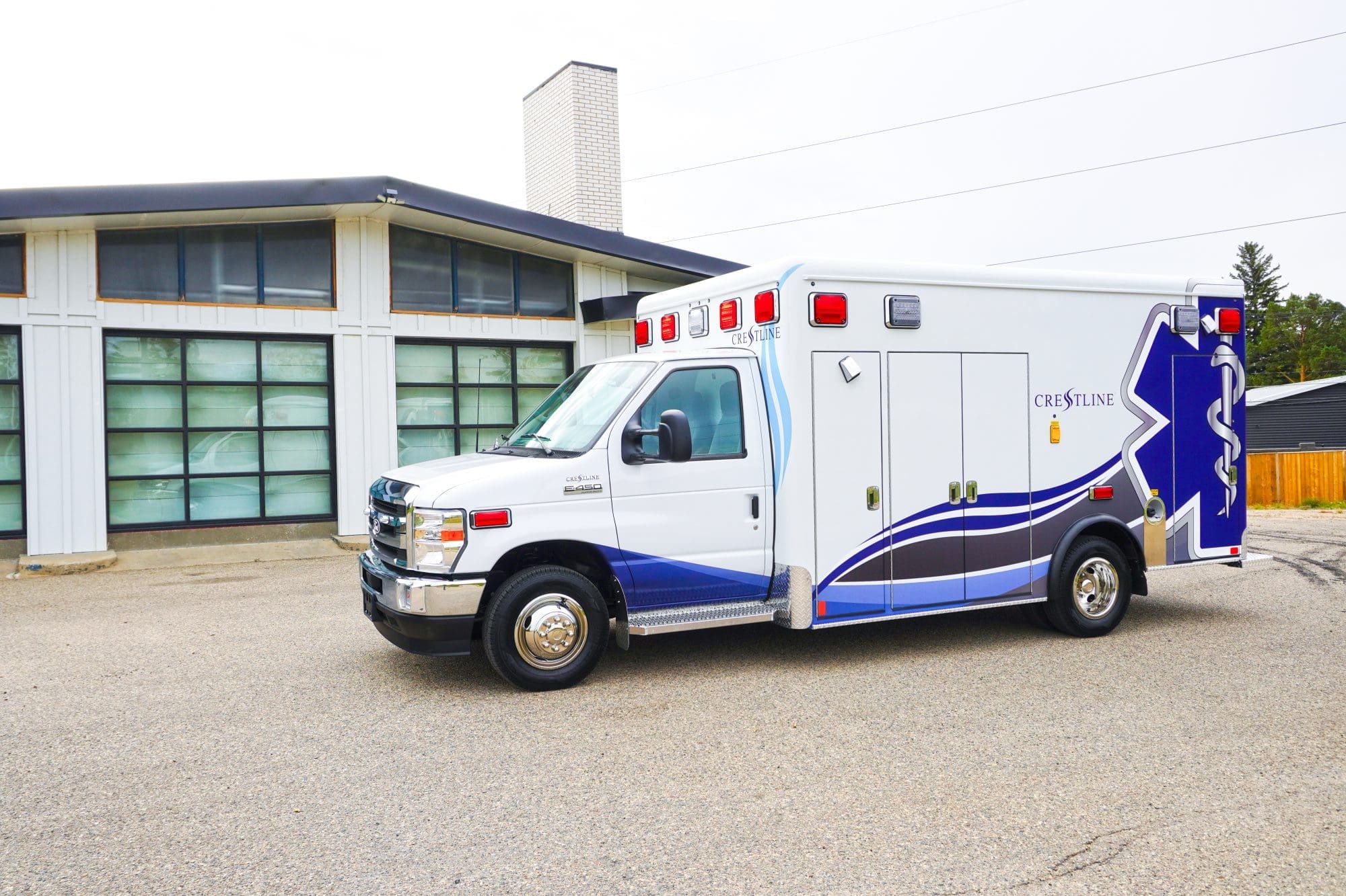 Crestline CCL 166 ambulance parked outside a modern building, featuring a clean white exterior with blue and gray graphics and the Crestline logo on the module side
