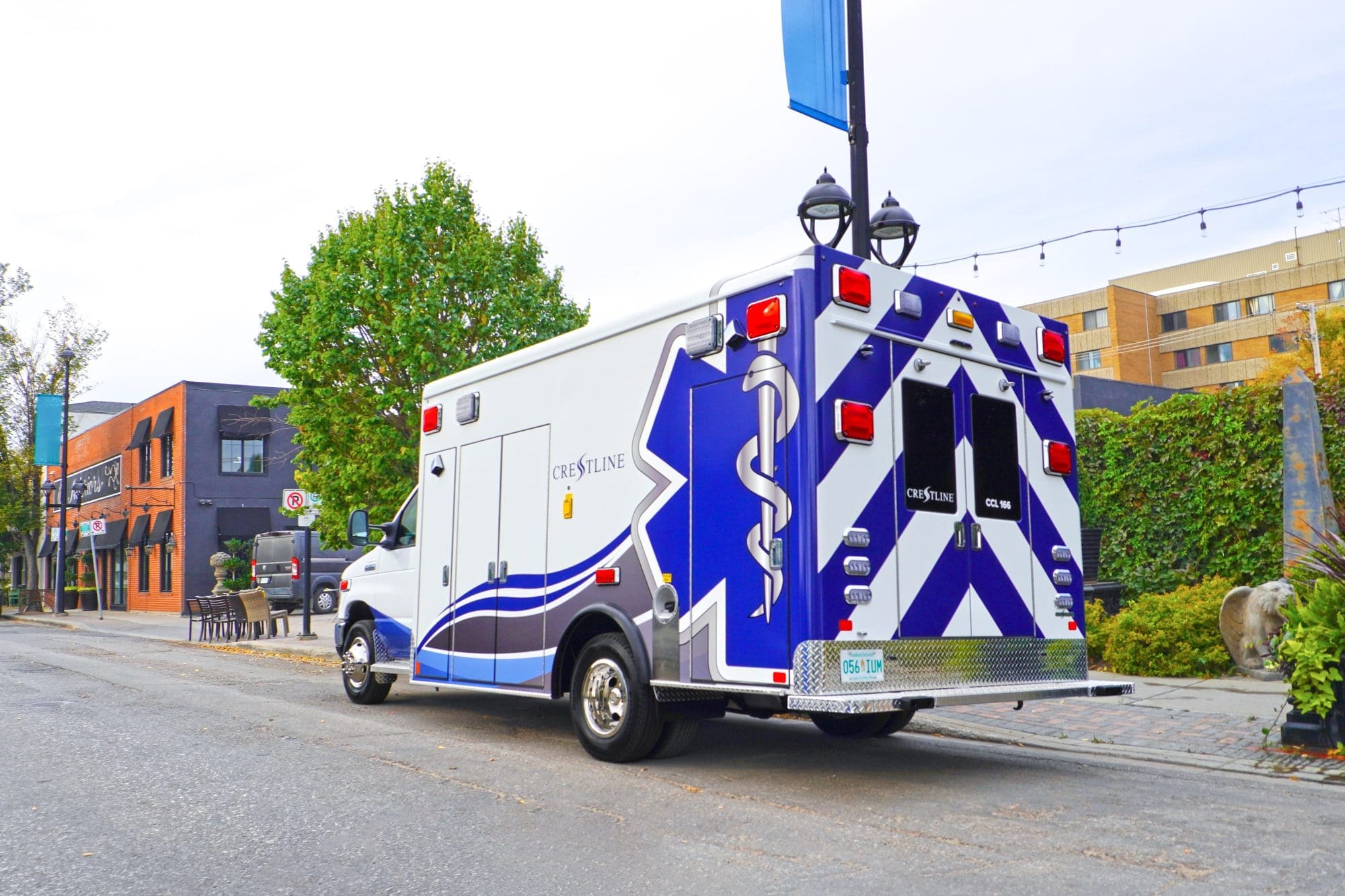 Crestline CCL 166 ambulance parked along a city street, displaying its rear and side graphics with buildings and trees in the background