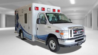White Crestline Ford E-350 ambulance with red emergency lights parked indoors in a well-lit garage
