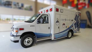 Side view of a Ford E350 ambulance with red emergency lights, Crestline branding, and a large blue Star of Life graphic, displayed indoors