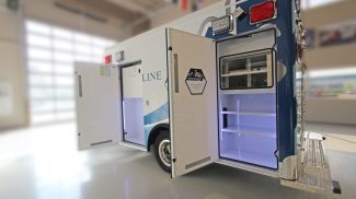 Open exterior compartments on a Crestline ambulance, showing illuminated storage spaces with shelving for medical equipment and supplies