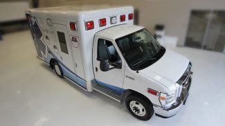 Angled overhead view of a white Crestline ambulance with red emergency lights and blue side graphics, parked indoors on a glossy white floor