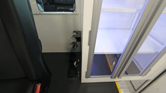 Interior of a Crestline ambulance showing a black attendant seat next to a partition wall with sliding glass doors and a mounted storage rack for securing oxygen cylinders