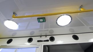Interior ceiling view of a Crestline ambulance showing bright round LED dome lights, overhead yellow safety rail, and ventilation outlets