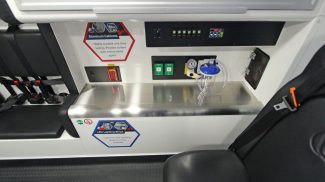 Interior view of an ambulance workstation with stainless steel countertop, oxygen controls, and electrical outlets