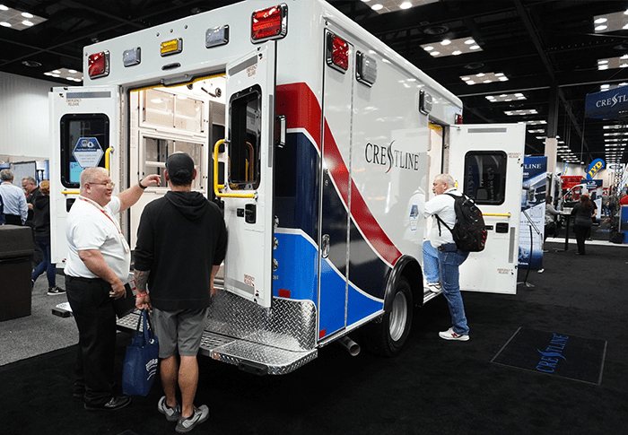 ccl-166-ambulance-dealers Attendees explore a Crestline ambulance on display at an industry trade show, viewing the vehicle’s rear patient area while speaking with company representatives on the exhibit floor